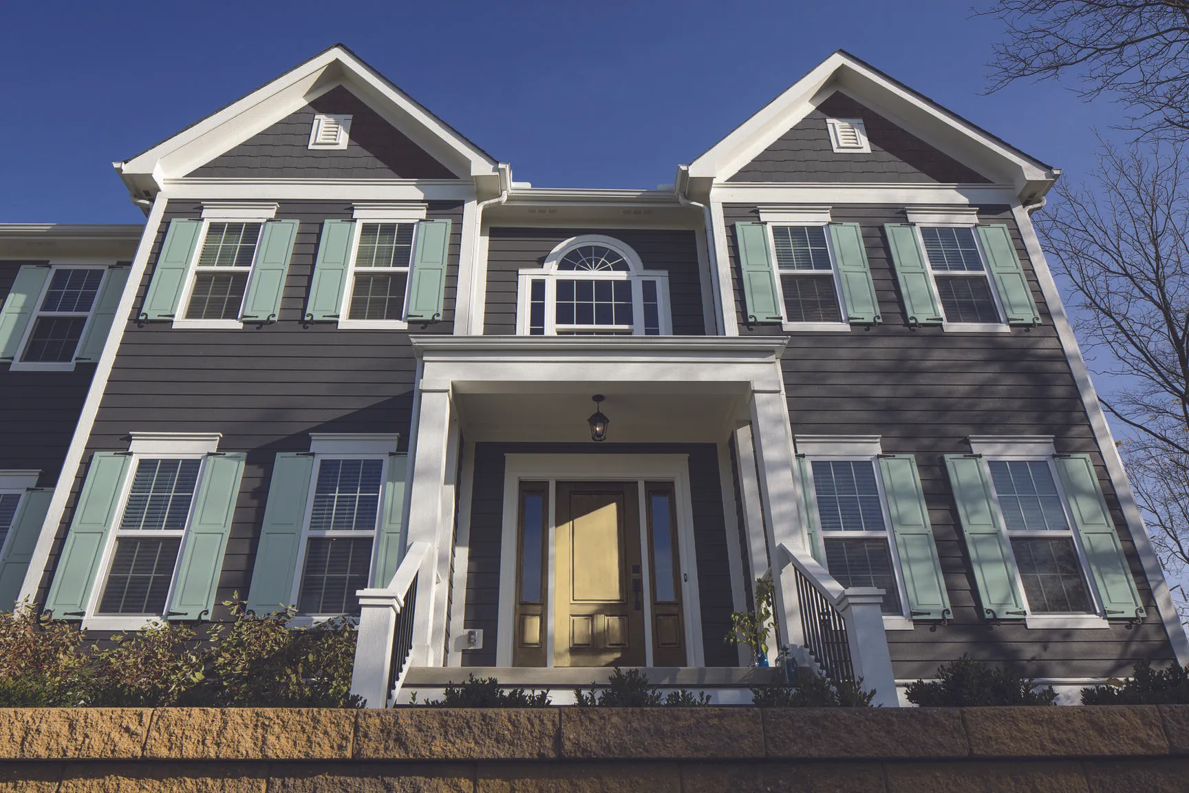 Two-story house with gray siding, white trims, green shutters, and a golden front door under a porch.